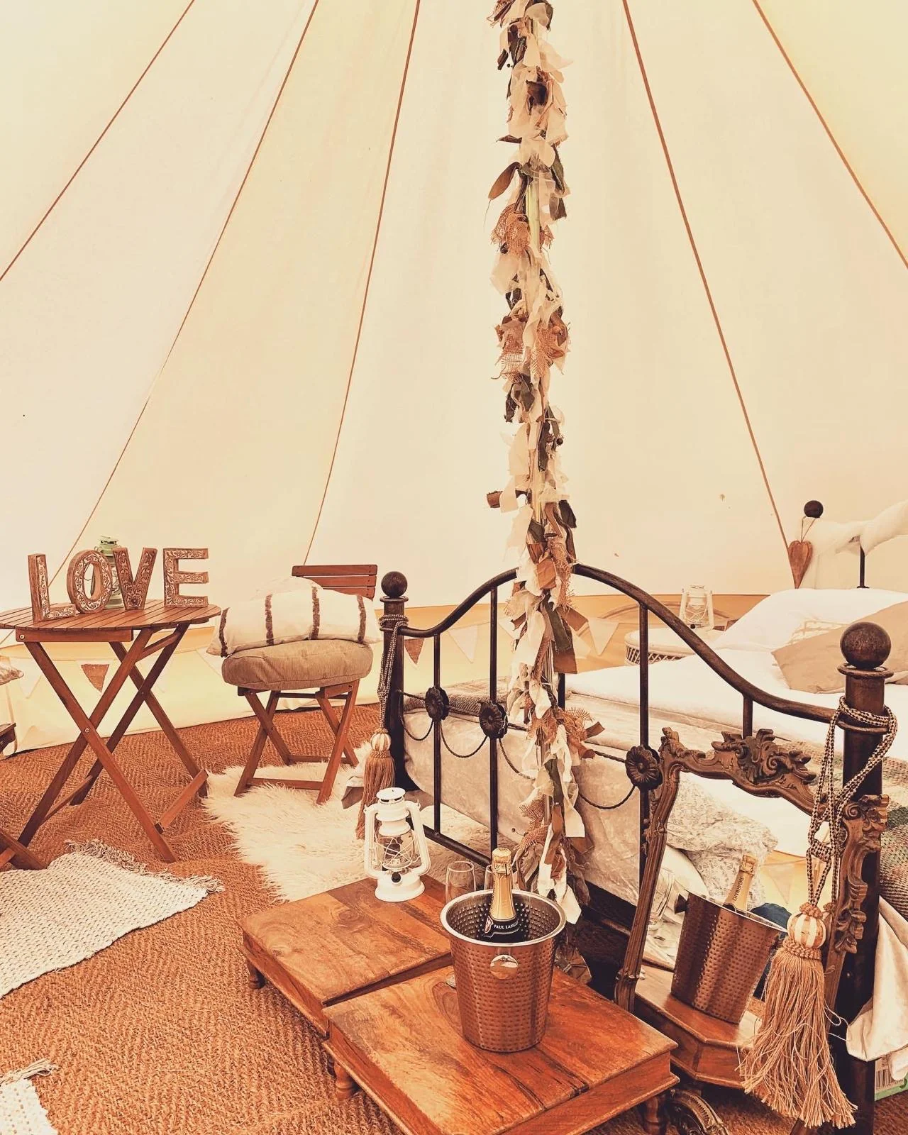 Romantic bell tent setup with iron bed and champagne